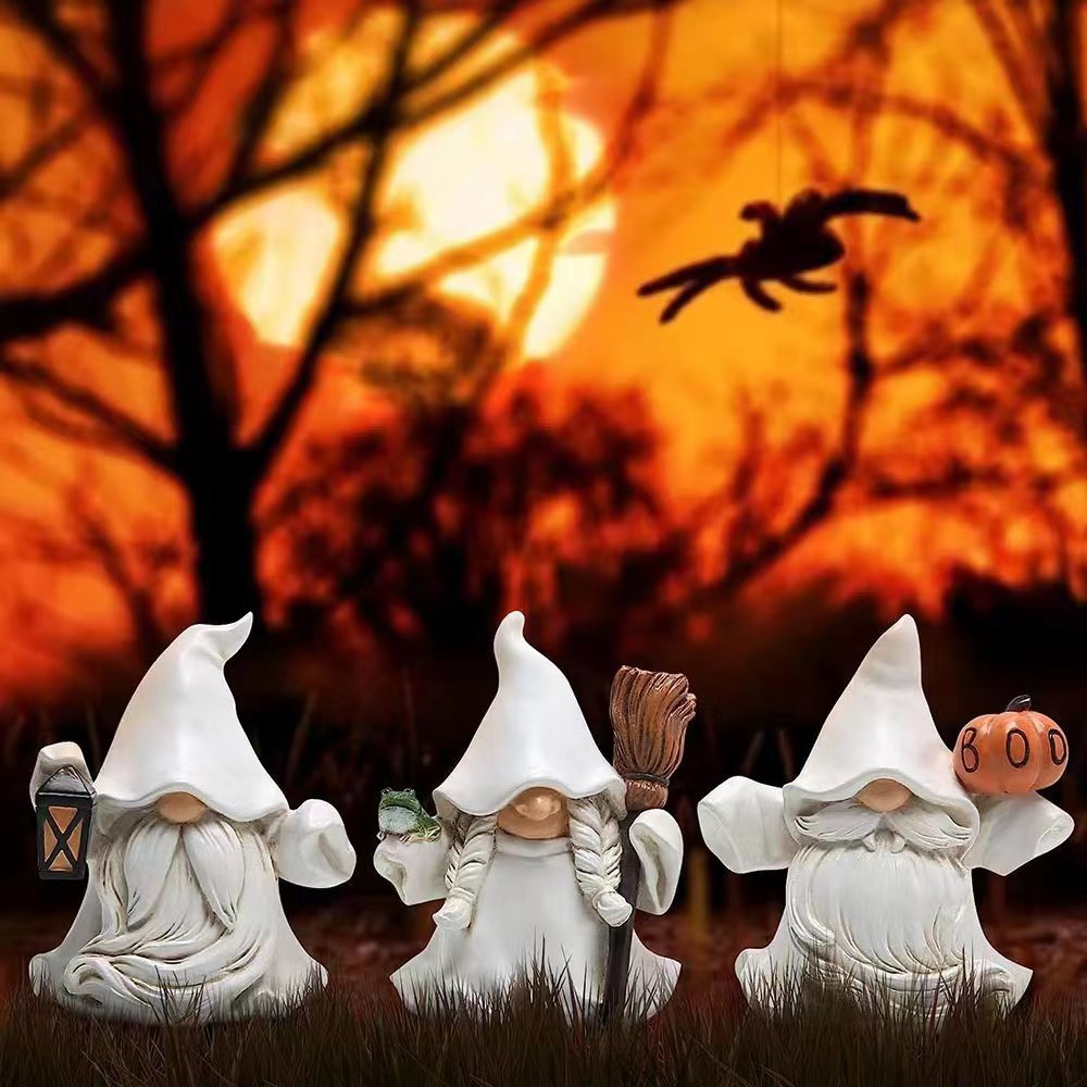 Three gnome figures in ghost costumes stand in grass against a fiery orange sky with a large moon and silhouetted trees. A hanging spider adds to the Halloween theme.