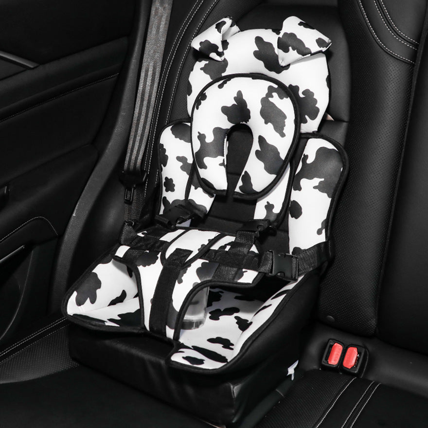 Car seat with a black and white cow pattern, featuring a cushioned headrest and secure straps, set on a dark interior of a vehicle.