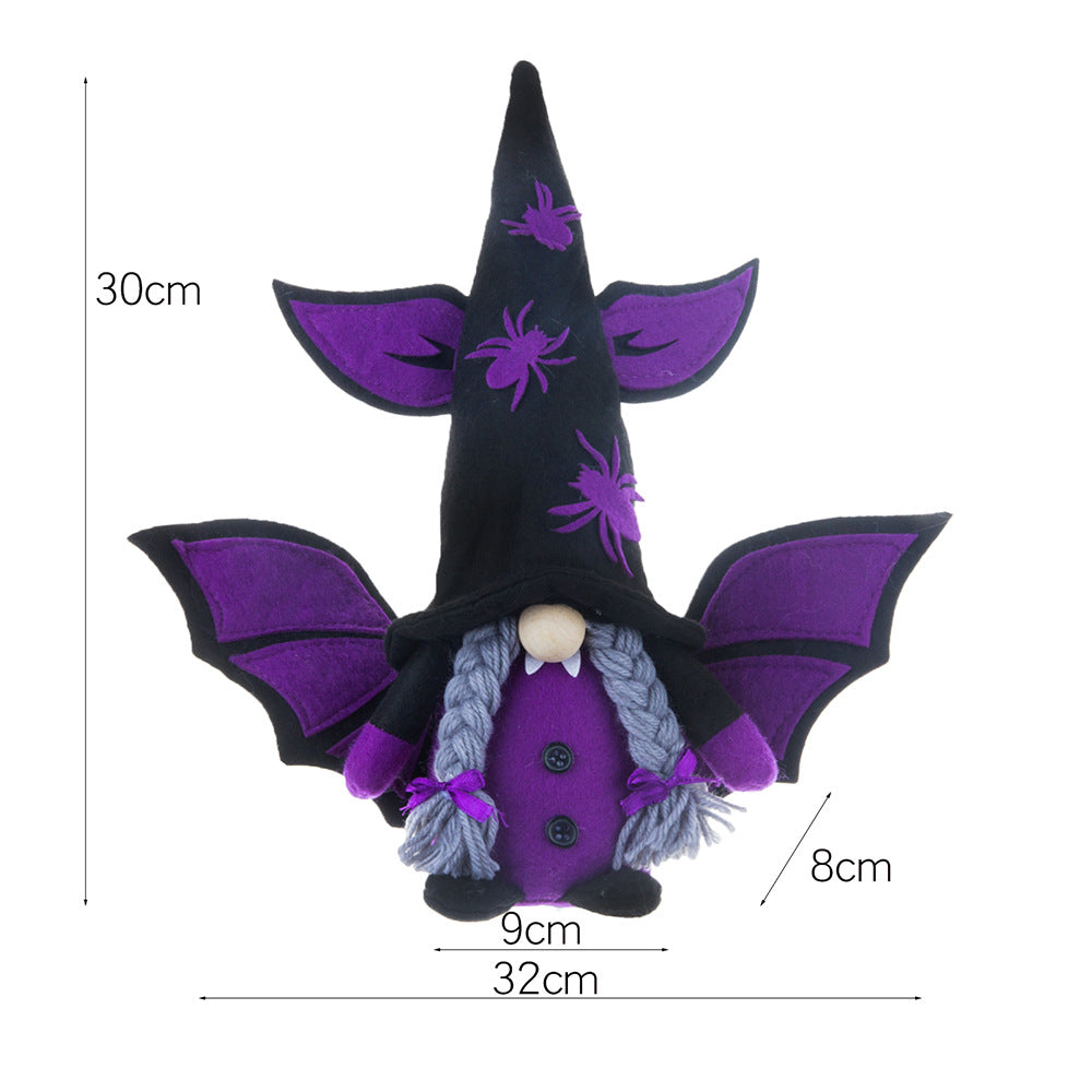 A whimsical purple gnome doll dressed as a witch, featuring a tall black hat adorned with purple spiders and bat-like wings. The gnome has grey braids and a round nose. Dimensions are 30cm tall, 32cm wide including the wings, and 9cm at the base.
