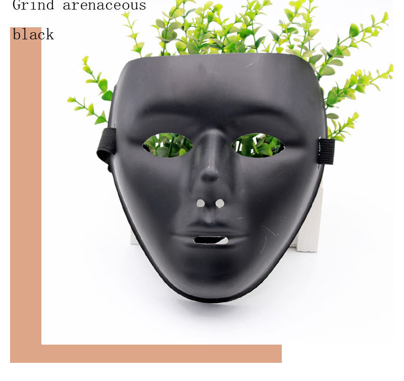 A matte black face mask rests against a planter with green foliage, set against a white background. Text in the top left reads "Grind arenaceous black."