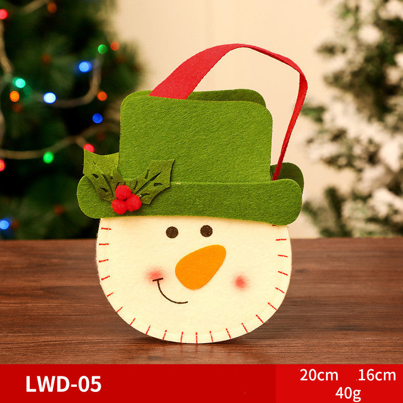 Festive felt snowman bag with green hat, red handle, and holly decoration, set on a wooden table with a blurred Christmas tree in the background. Dimensions: 20cm x 16cm, 40g.