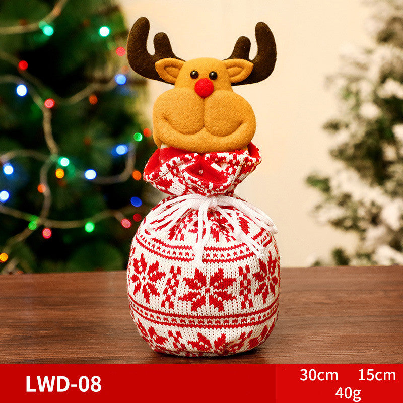 Festive holiday decoration featuring a plush reindeer head atop a red and white knitted sack. Background shows blurred Christmas lights and a tree. Dimensions and weight listed below.