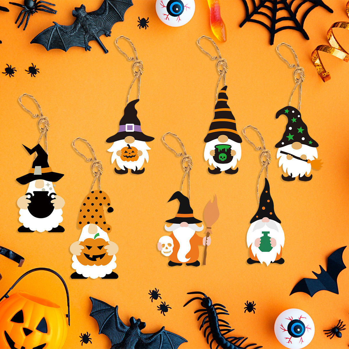 A Halloween-themed image featuring seven keychains shaped like gnomes wearing witch hats, holding various spooky items like pumpkins and cauldrons. The background is orange with decorative elements such as bats, spiders, eyeballs, and a jack-o'-lantern, creating a festive atmosphere.