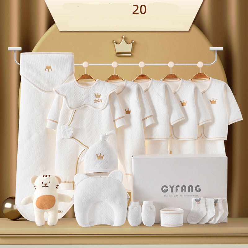 A set of white baby clothing with crown embroidery, including outfits, hat, and mittens, displayed on hangers. Accompanied by a plush toy and a gift box.
