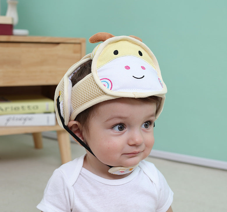 A child wearing a cute, animal-themed protective headgear featuring a smiling face. The background includes a wooden table with books and a green wall.