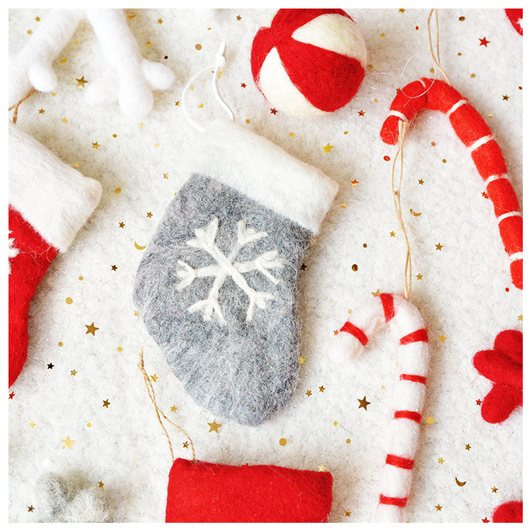 Festive felt decorations on a white surface include a gray stocking with a snowflake, red and white candy canes, a ball, and sprinkled with gold stars.