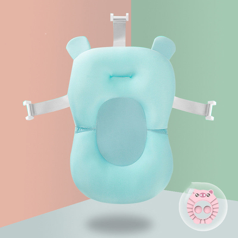 Light blue baby bath cushion with head support, designed to secure in a tub using adjustable white straps. Background is split into pink and green halves. Small pink animal-themed accessory in corner.