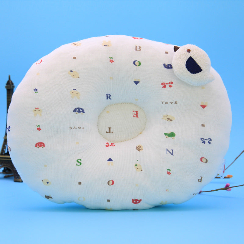 Round white pillow with colorful letters, toys, and animal illustrations. Features a small, plush bird on top. Set against a light blue background with a miniature Eiffel Tower.
