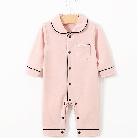 Pink baby jumpsuit with black piping, long sleeves, and buttons down the front. Features a small front pocket and is displayed on a wooden hanger against a white background.