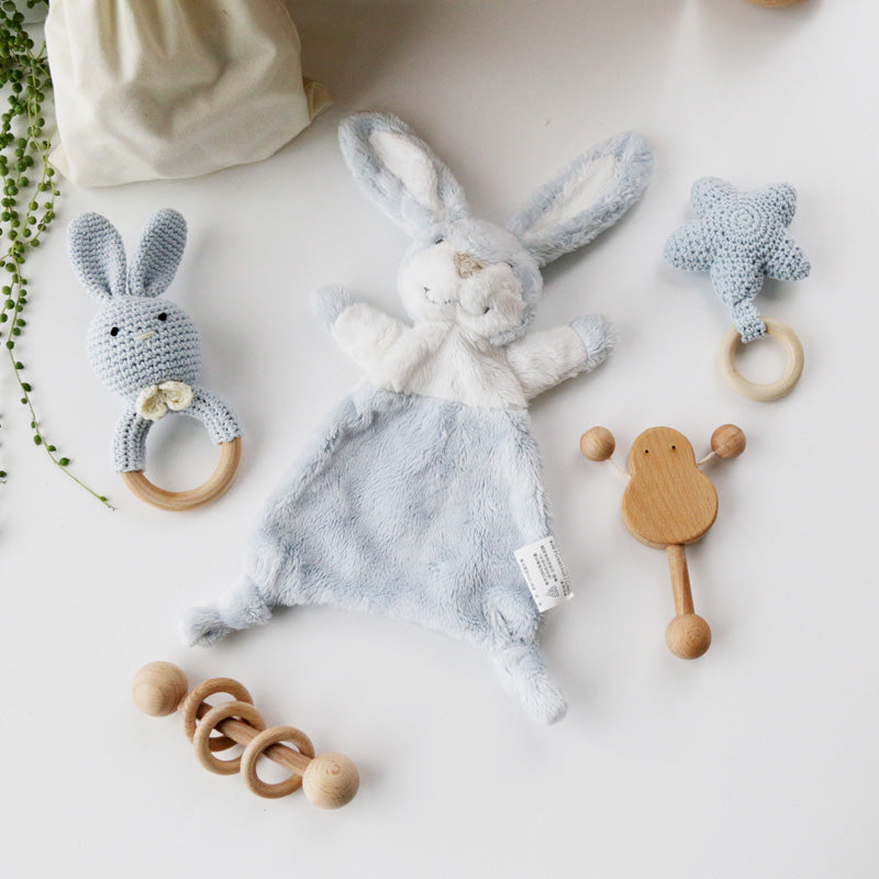 Plush bunny toy and crocheted star and bunny rattles on a white surface. Wooden toys, including a rattle and teether, complete the playful ensemble.