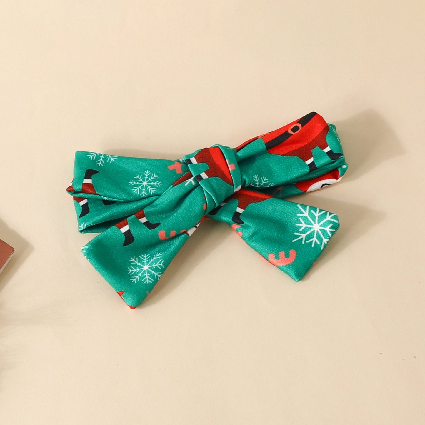 Green festive bow tie with red and black reindeer pattern and white snowflakes, neatly tied against a light beige background.