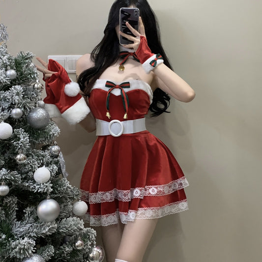 Woman in a red and white Christmas-themed dress with lace and bows poses by a decorated Christmas tree. She is taking a mirror selfie with a smartphone.