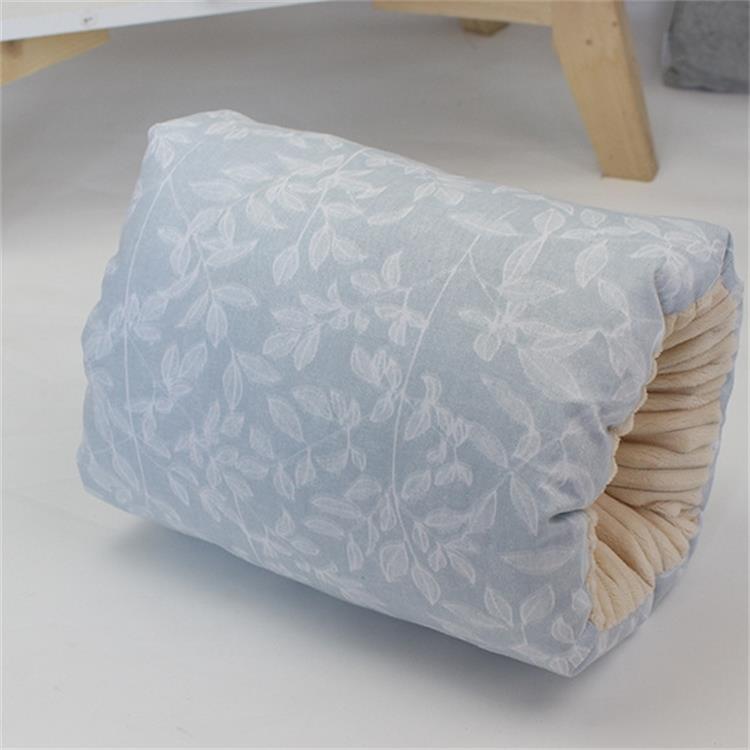 A bolster pillow with a light blue cover featuring a subtle white leaf pattern lies on the floor. The pillow's end is lightly pleated, showing a beige lining inside.