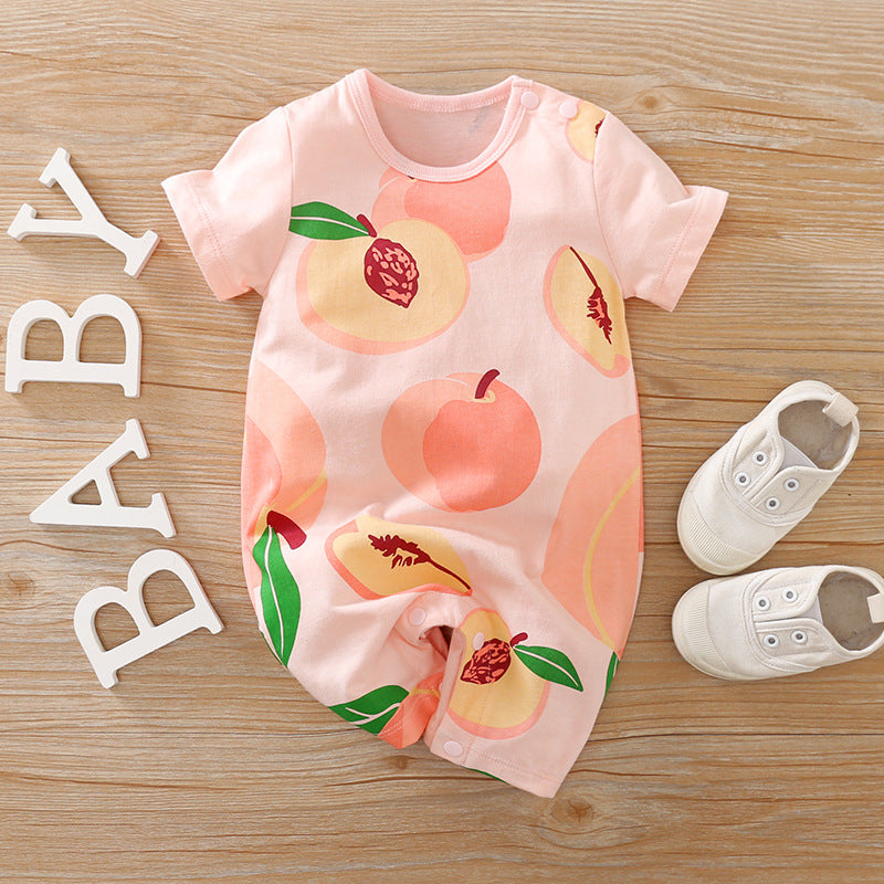 Pink baby romper with peach patterns, placed on wooden surface next to white baby shoes and white letters spelling "BABY."