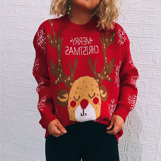 Child wearing a red Christmas sweater with a reindeer design and snowflakes. The text "Merry Christmas" is visible but reversed, seen against a white textured wall.