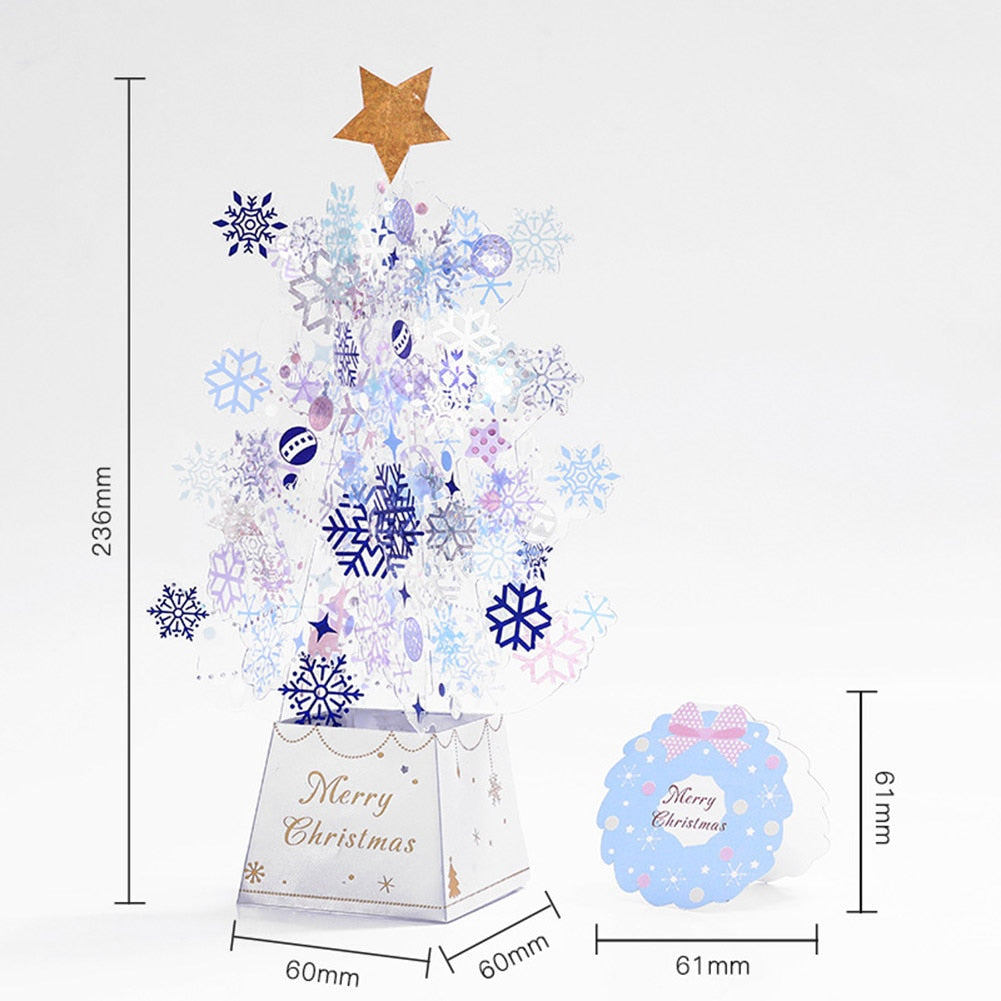 Snowflake-themed paper Christmas tree with a golden star topper, measuring 236mm tall and 60mm wide. "Merry Christmas" is printed on the base. A small blue card accompanies it.