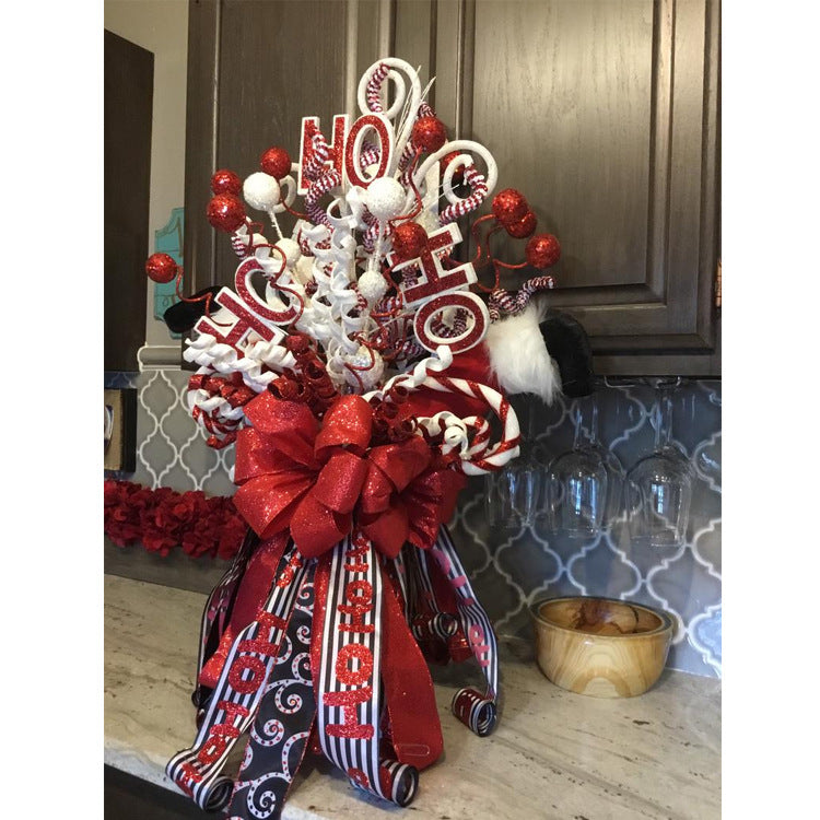 Festive Christmas arrangement with red and white decorations, featuring glittery "Ho Ho Ho" signs, curly ribbons, candy canes, and a large red bow on a kitchen counter.