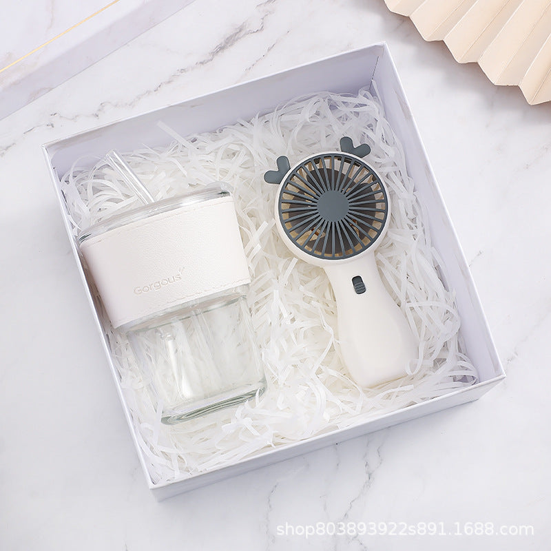 Gift box with a clear glass tumbler and a white handheld fan, both placed on crinkled paper shreds. The tumbler has a white sleeve labeled "Gorgeous" and a straw.