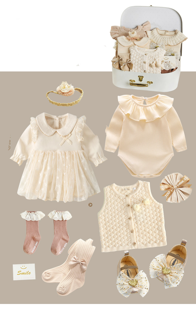 Baby clothing set in soft beige tones, including a dress, bodysuit, vest, socks, shoes, and a headband, neatly arranged beside a suitcase with more clothes.