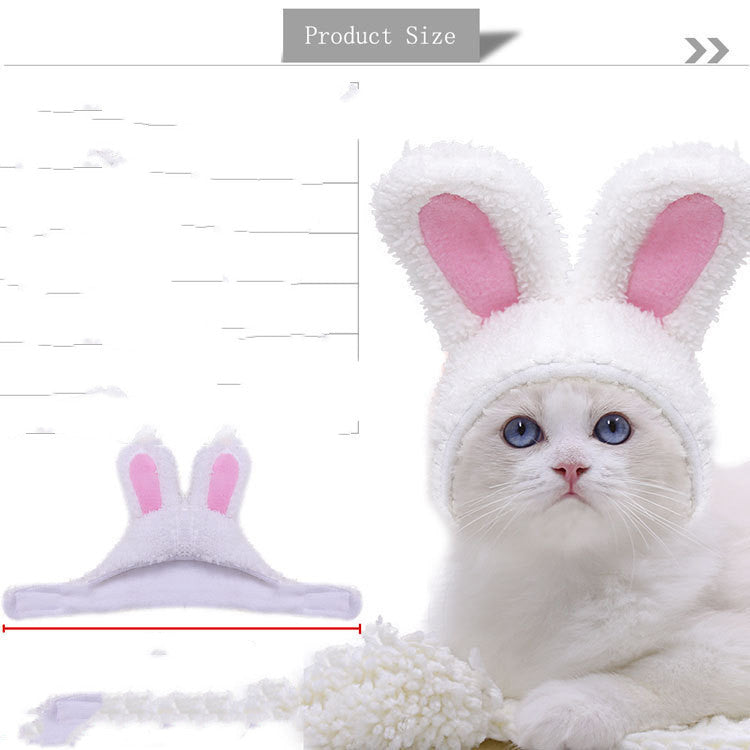 White cat wearing a fluffy hat with pink-lined bunny ears. Hat shown separately with measurements indicating product size. Background is white with light shadows.
