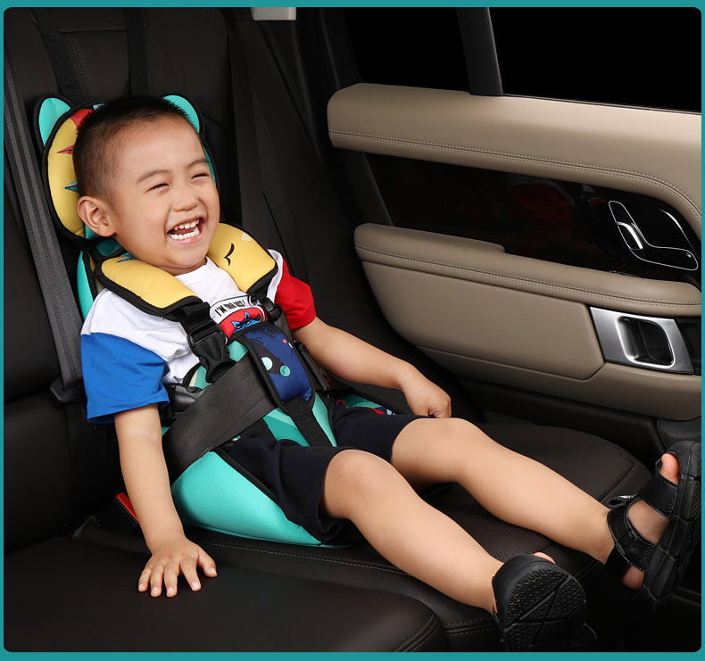 A smiling child in a colored shirt and black shorts sits in a car seat with a padded headrest. The car seat is securely fastened in a vehicle's backseat.