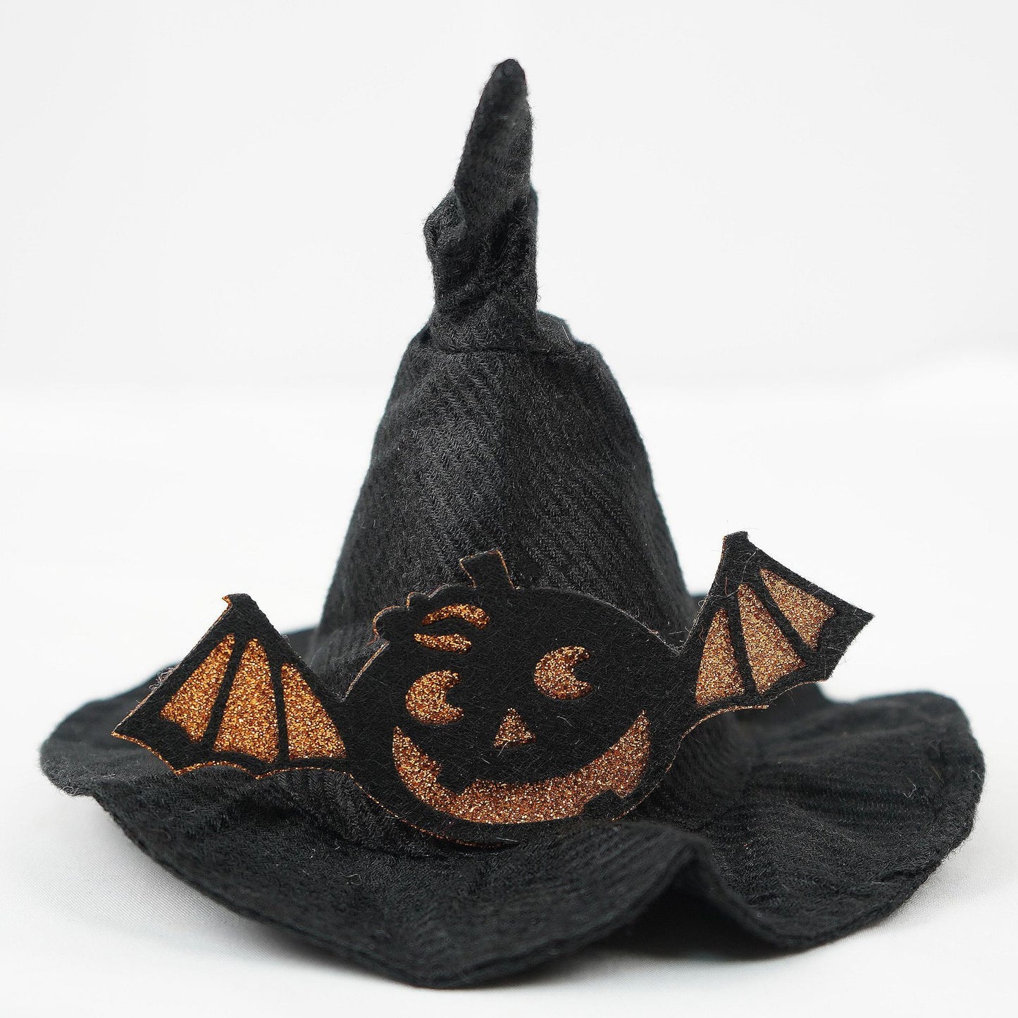 Black witch hat decorated with a glittery orange jack-o'-lantern face and bat wings on a plain white background, creating a spooky Halloween theme.