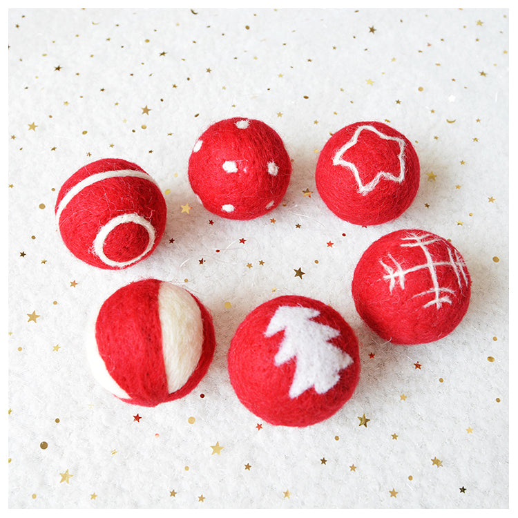 Six red felt balls with white patterns, including stars, stripes, dots, and a Christmas tree design, arranged in a circle on a white background with gold stars.
