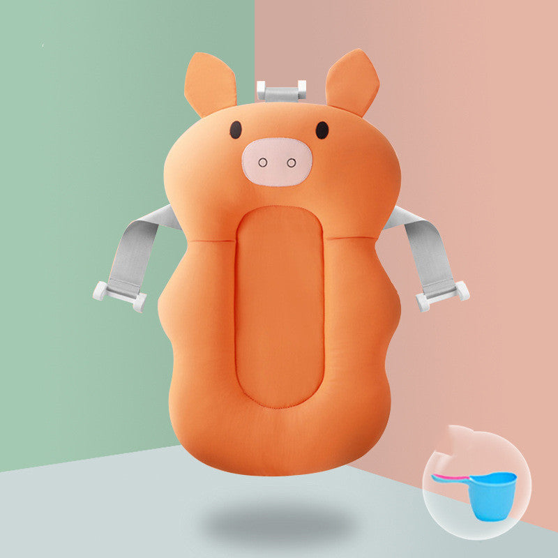 Orange pig-shaped baby bath cushion with gray straps, designed for comfortable support. A small blue scoop with a pink handle is shown in the bottom right corner.