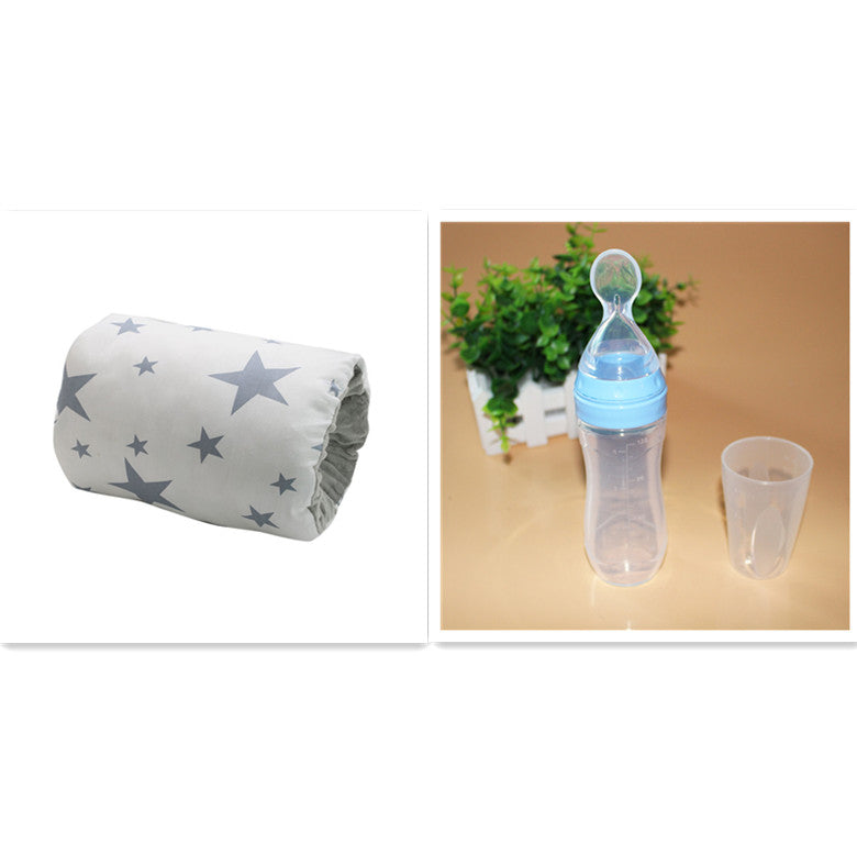 Rolled-up star-patterned fabric on the left; clear baby bottle with blue cap and a transparent cup on the right, set against a tan background with green plant decor.