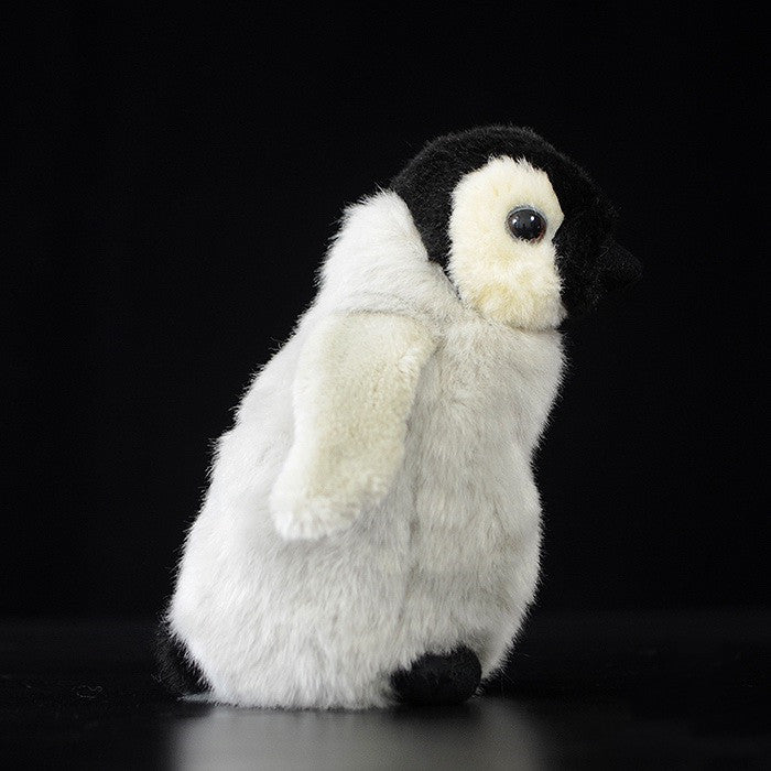 A plush penguin toy with a white body, black head, and flippers, stands on a black surface against a dark background, captured from a side profile.