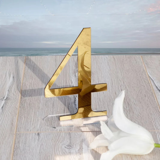 Gold number 4 on a wooden surface with a white flower nearby, set against a serene ocean backdrop with a cloudy sky.