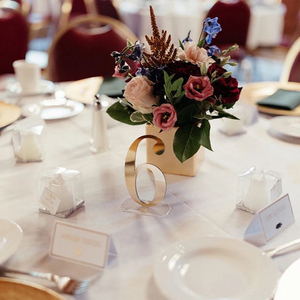 Elegantly set table with a floral centerpiece, a gold table number 6, and place cards. White tablecloth, red chairs, and small gift boxes add a formal touch.