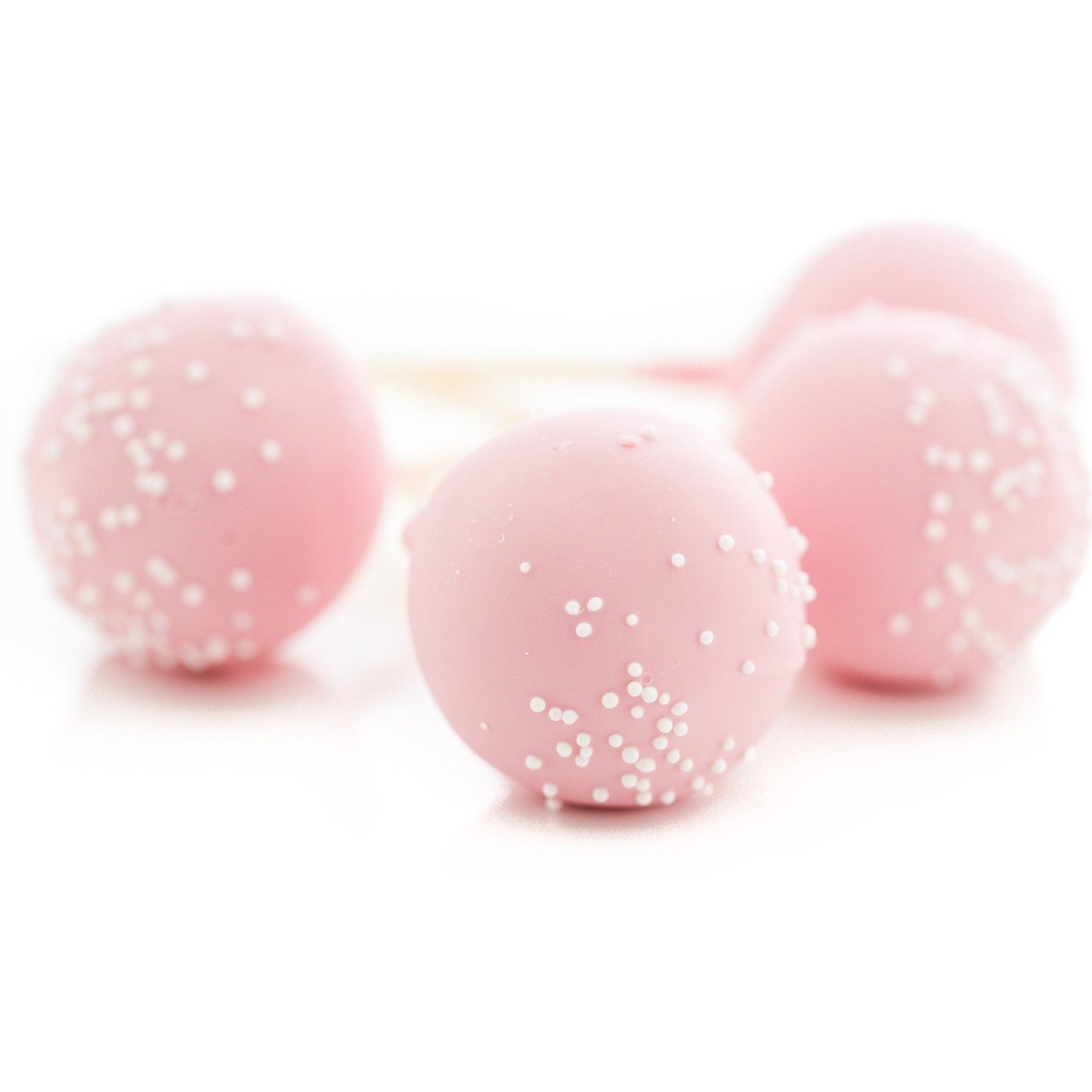 Four pink cake pops with white sprinkles are arranged closely together on a white background, creating a soft and appetizing appearance with a focus on one pop in the foreground.