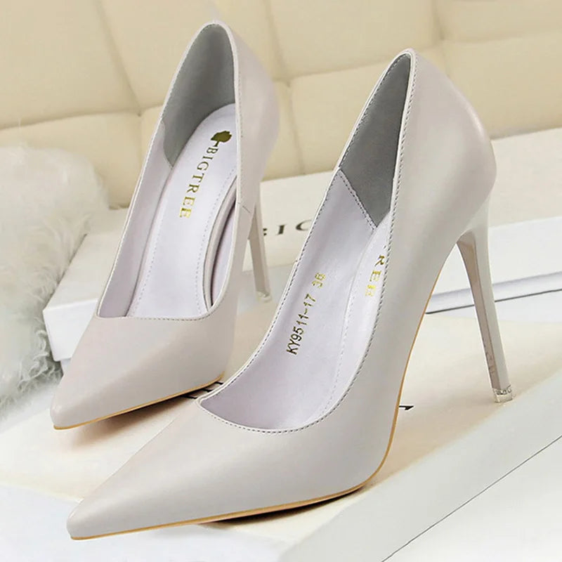 Elegant high-heeled shoes in a light beige color with pointed toes, displayed on a soft background. The brand name is visible on the inner sole.