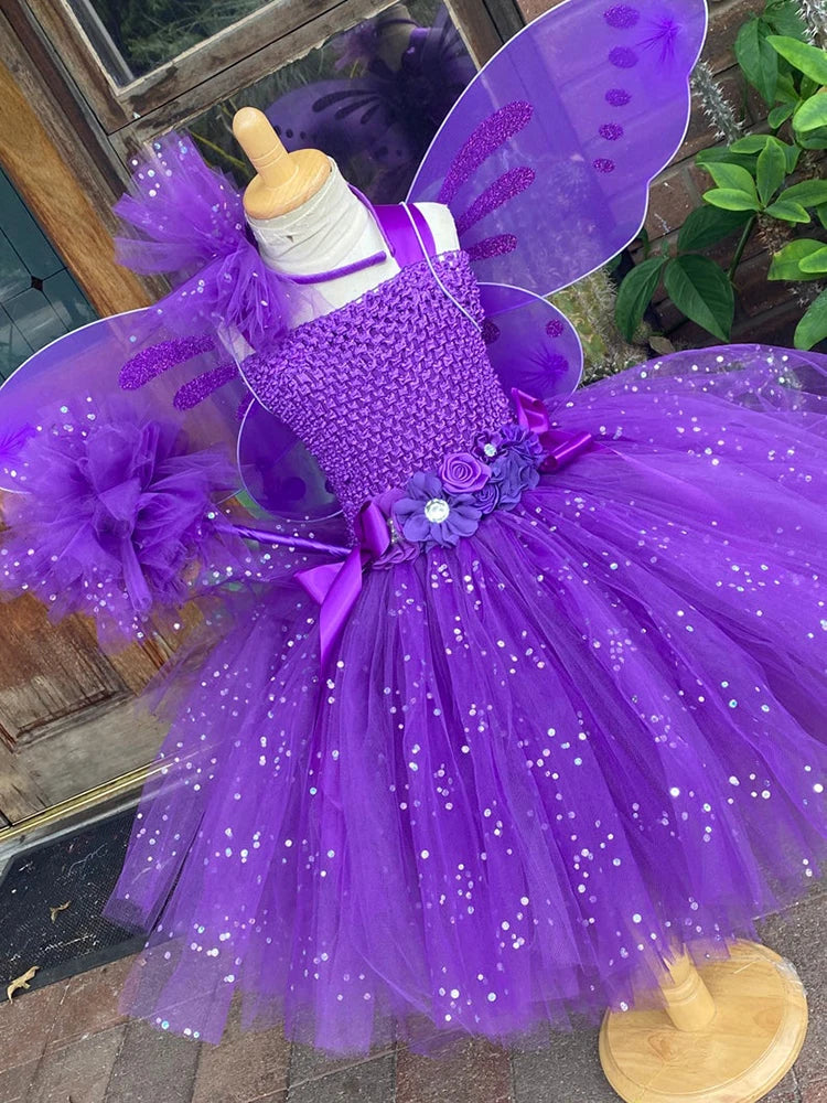 Purple fairy costume on a mannequin featuring glittery wings, a flower-adorned bodice, and a tulle skirt with shimmering sequins. It's displayed outdoors near a wooden door.