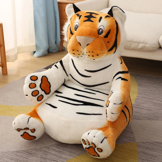 A large, plush tiger stuffed animal with orange and black stripes sits on a patterned rug in a cozy living room with a light-colored sofa and curtain in the background.