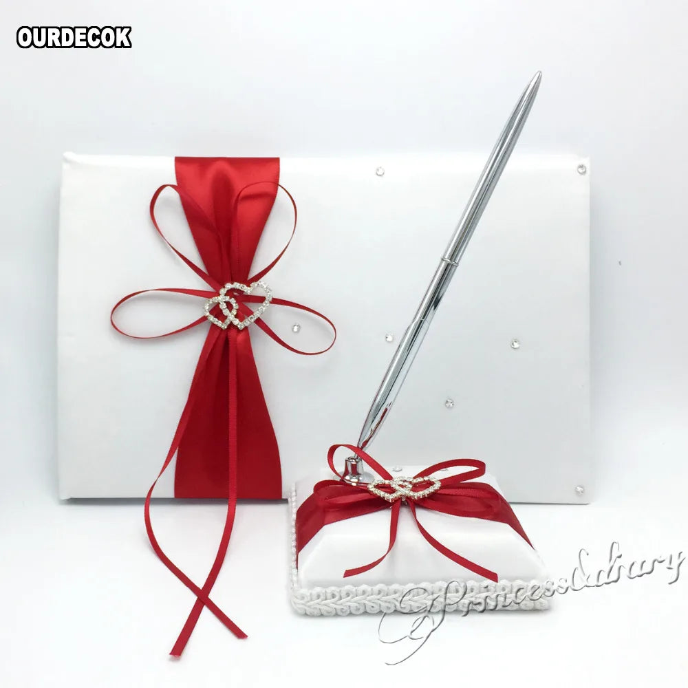Elegant wedding guest book set featuring a white book adorned with red ribbon and rhinestone hearts, accompanied by a silver pen on a matching red and white base.