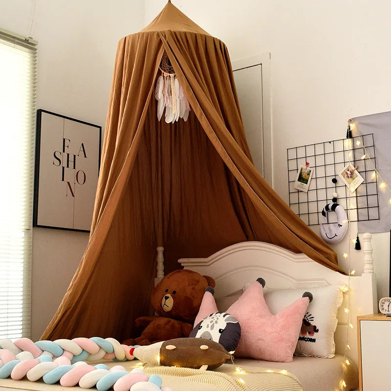 Cozy bedroom with a brown canopy over a bed featuring teddy bear and crown-shaped pillows. A fashion poster and string lights decorate the walls, adding a warm ambiance.