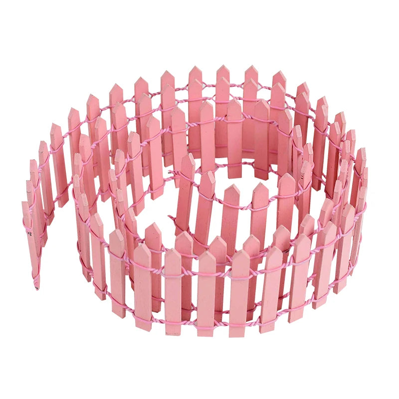 A roll of miniature pink picket fence, neatly coiled. The fence features pointed tops and is interconnected with pink wire, suitable for crafts or decorative garden setups.