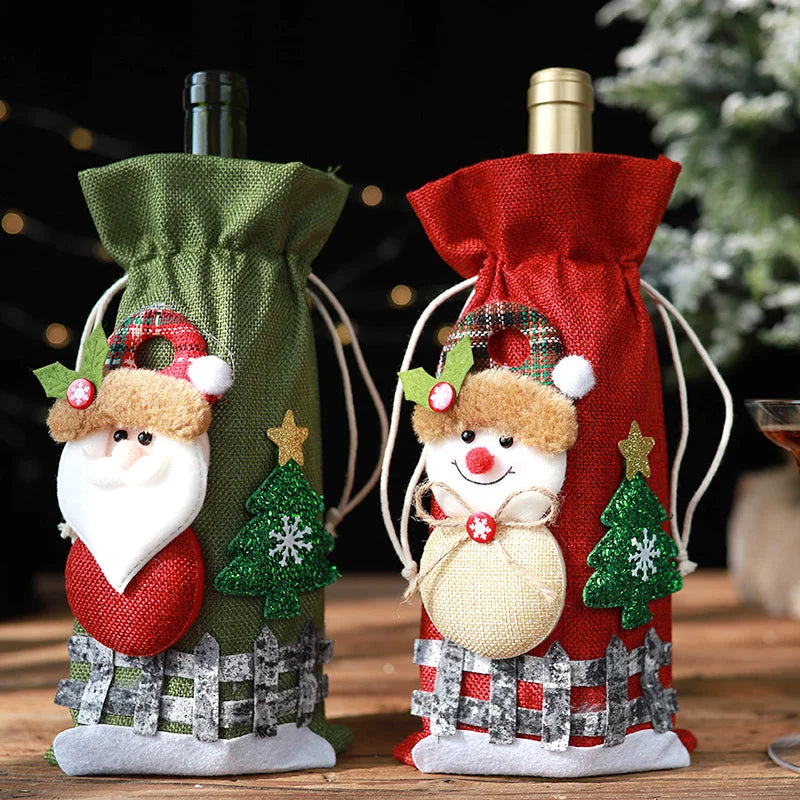Two wine bottles in festive green and red burlap bags, adorned with Santa and snowman decorations, green glittery trees, and star embellishments, set on a wooden surface.