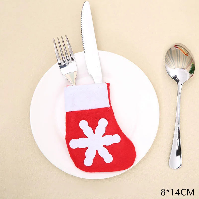 Red felt stocking-shaped cutlery holder with a white snowflake design on a plate, holding a fork and knife. A spoon is placed beside the plate. Dimensions noted as 8x14cm.