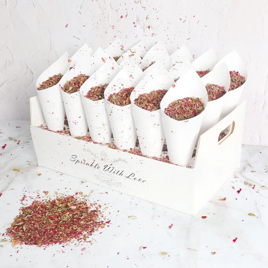 White cones filled with colorful dried flower petals arranged in a box labeled "Sprinkle With Love." Some petals are scattered on the marble surface below.
