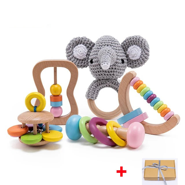 Wooden baby toys set including a crocheted elephant rattle, abacus with colorful beads, and ring stacker. A gift box tied with ribbon is also included.
