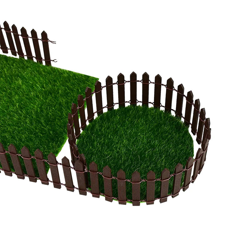 Miniature brown picket fence enclosing circular and rectangular patches of artificial green grass, set on a white background.