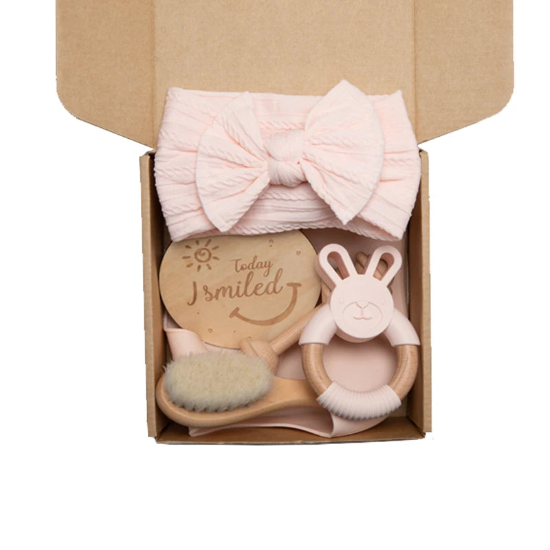 Gift box containing a pink bow headband, a wooden plaque with "Today I smiled" inscription, a soft-bristle brush, and a pink and wooden rabbit-shaped teether.