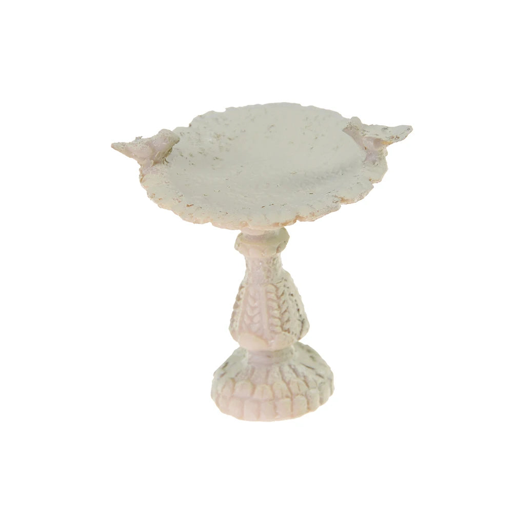 A small, ornate white birdbath with two bird figures perched on the rim and a textured pedestal base, set against a plain background.