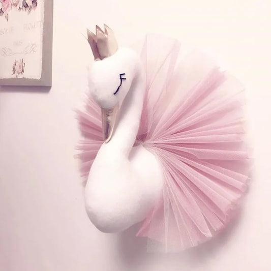 Plush white swan wall decoration wearing a gold crown and a pink tulle tutu, mounted on a light-colored wall near a floral artwork.