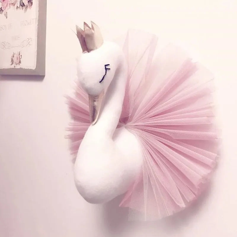 Plush swan wall decor with a golden crown and closed eyes, adorned with a fluffy pink tulle tutu, mounted on a white wall beside a floral art piece.