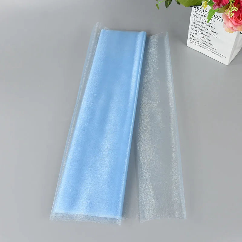 Folded blue and translucent fabric on a gray surface, next to a white vase containing pink flowers and a text-covered design.