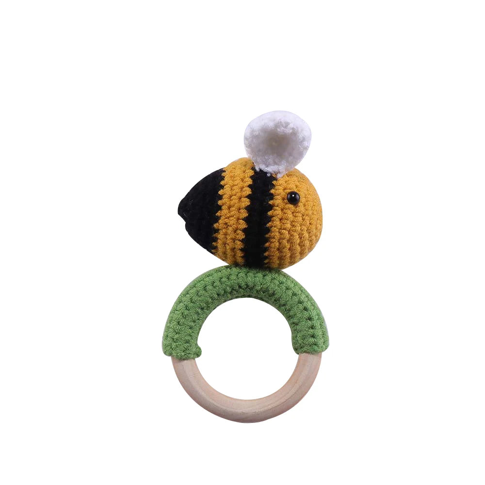 Crocheted bee baby rattle with a black and yellow-striped bee on top of a green, knitted ring and a wooden handle.